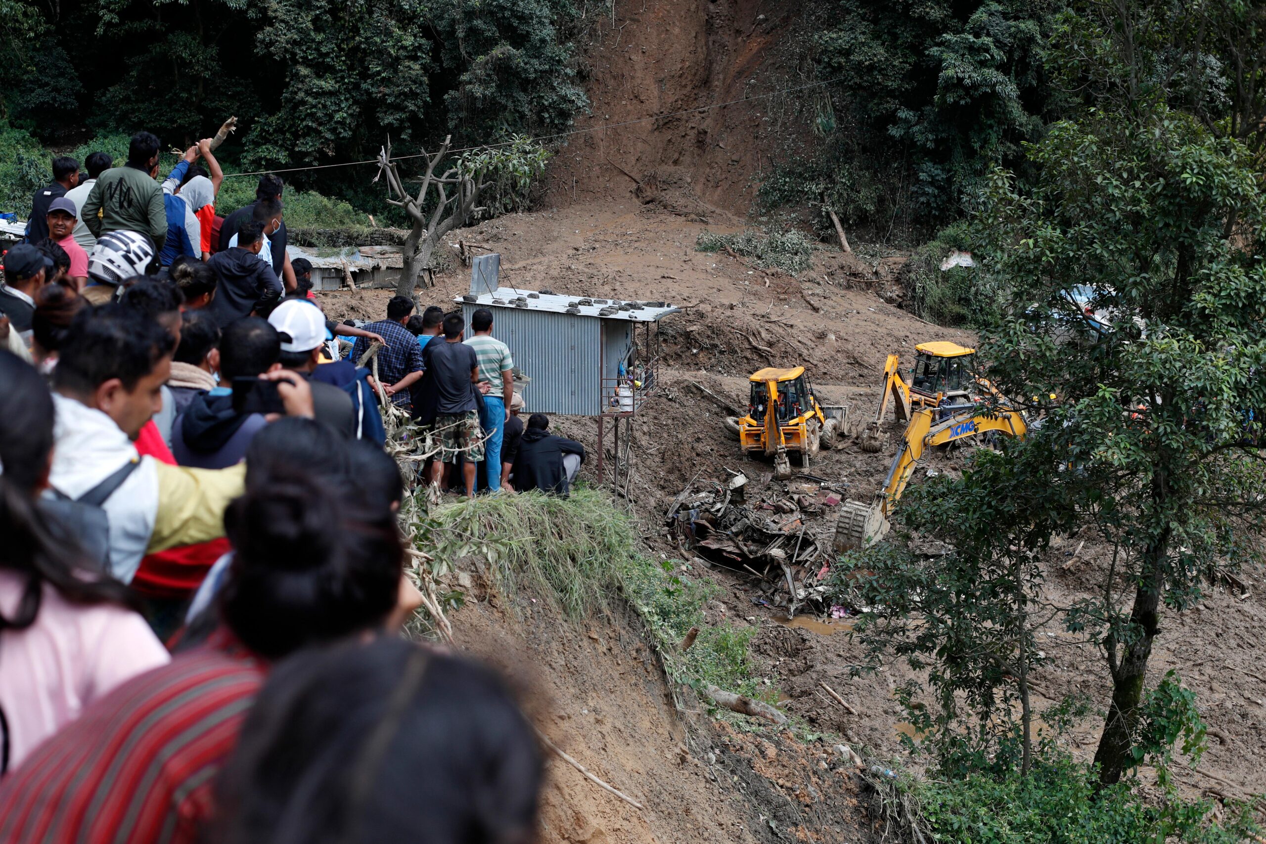 People watch earthmovers removing automobile debris and the dead bodies...