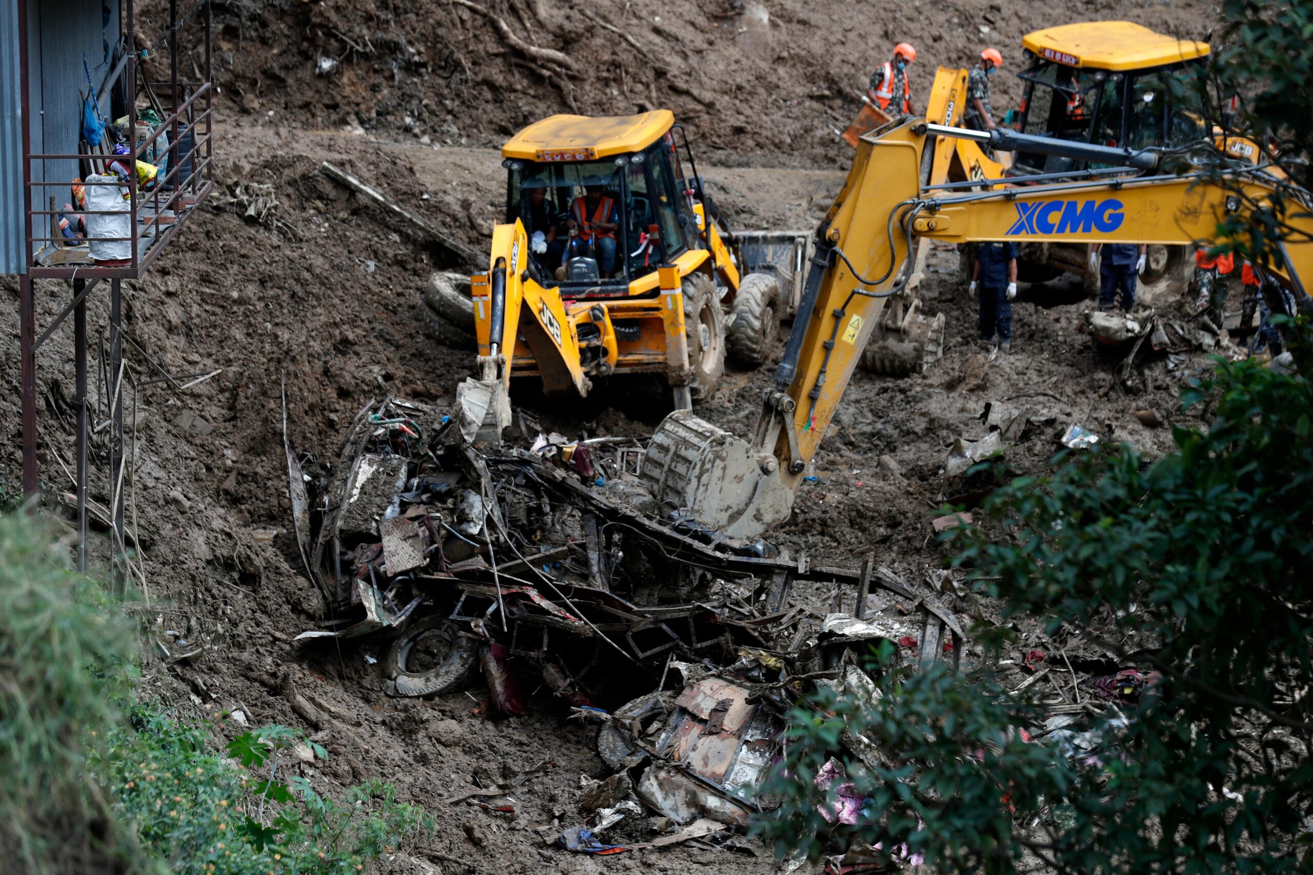 Earthmovers remove mangled automobile debris from a landslide caused by...