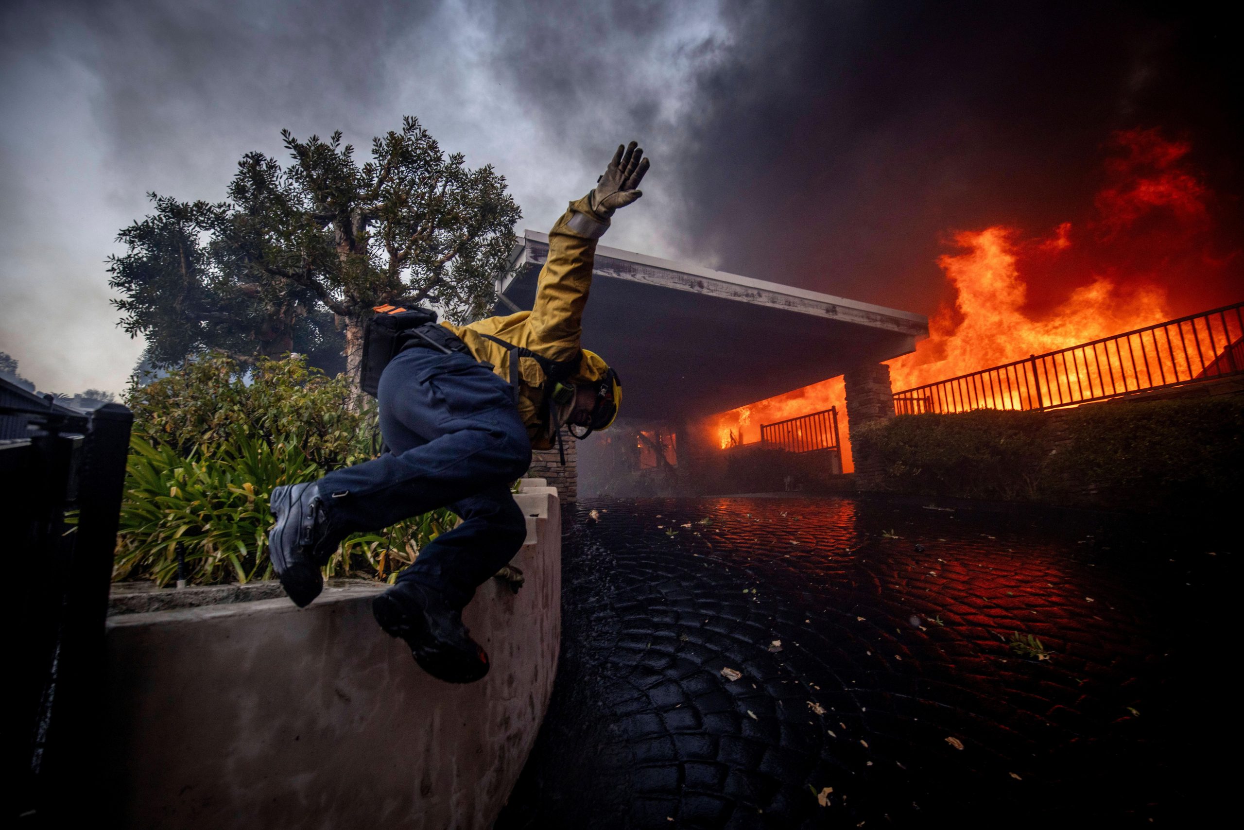 A firefighter jumps over a fence while fighting the Palisades Fire