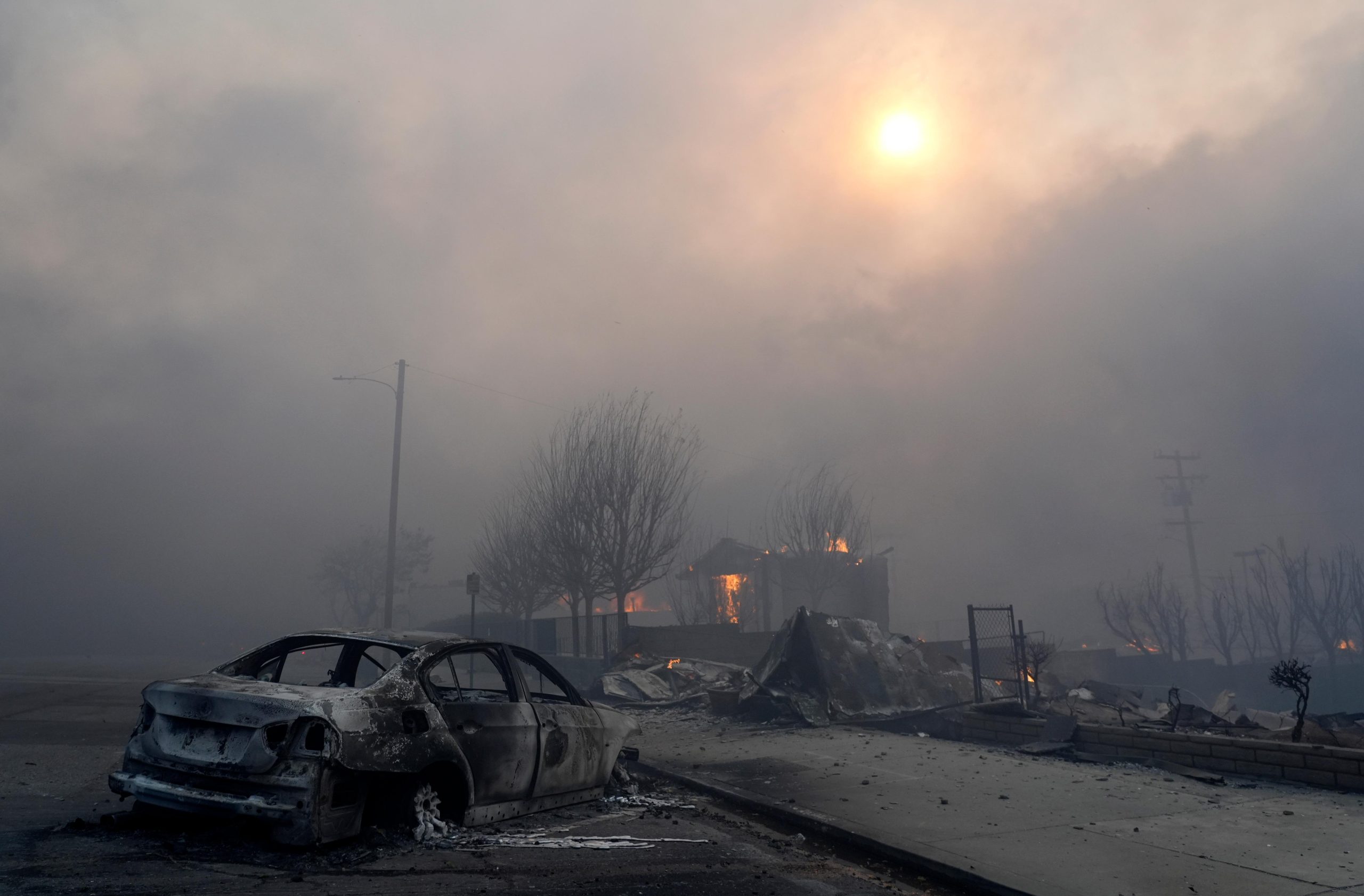 A burned-out car sits among rubble in the downtown Altadena...