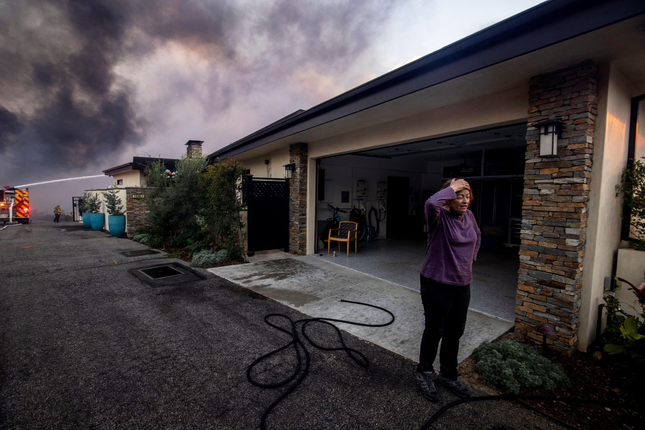 A resident stands in front of a garage as fire crews fight the Palisades Fire nearby