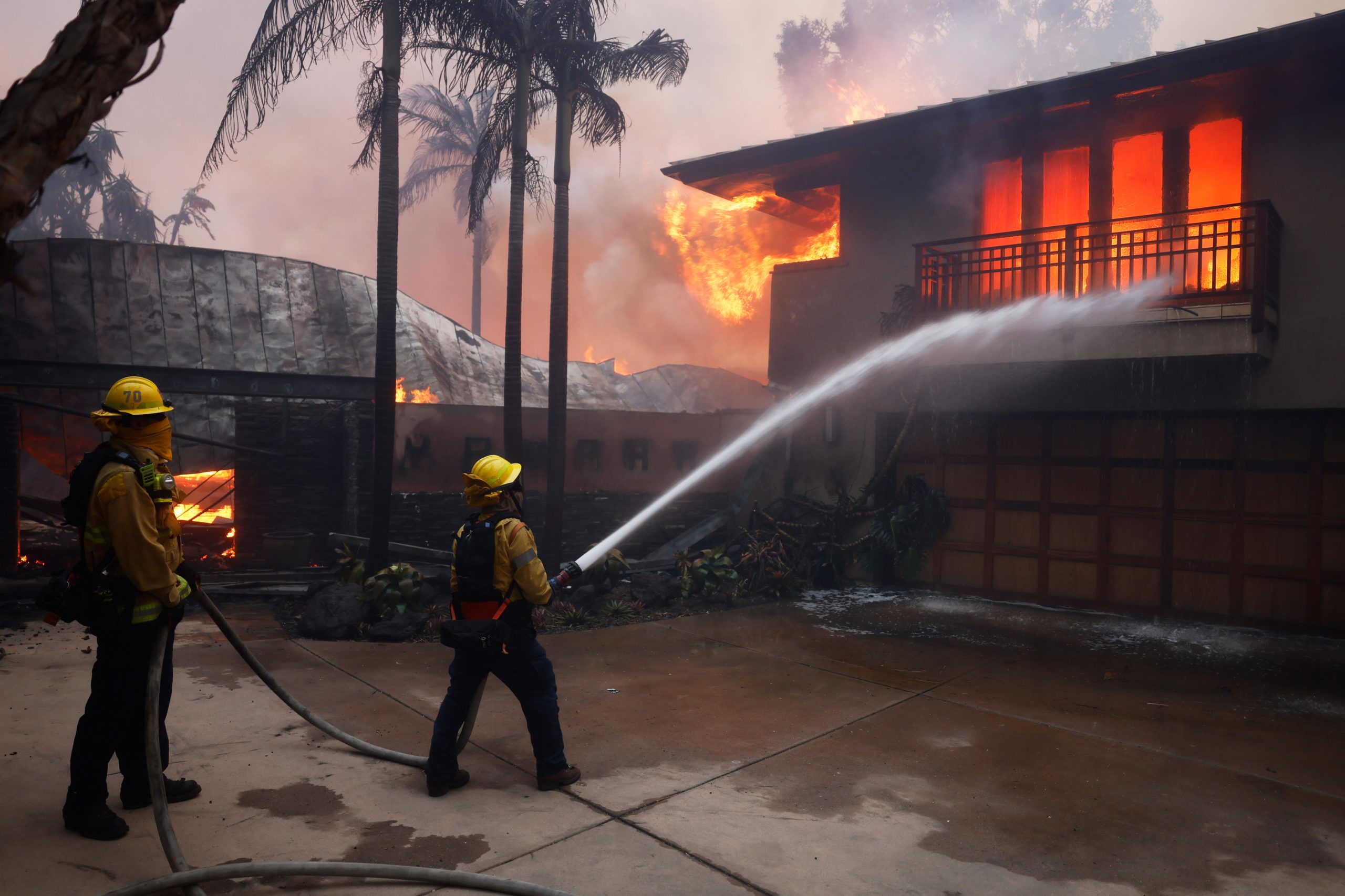 Firefighters hose down flames as the Palisades Fire destroys a...