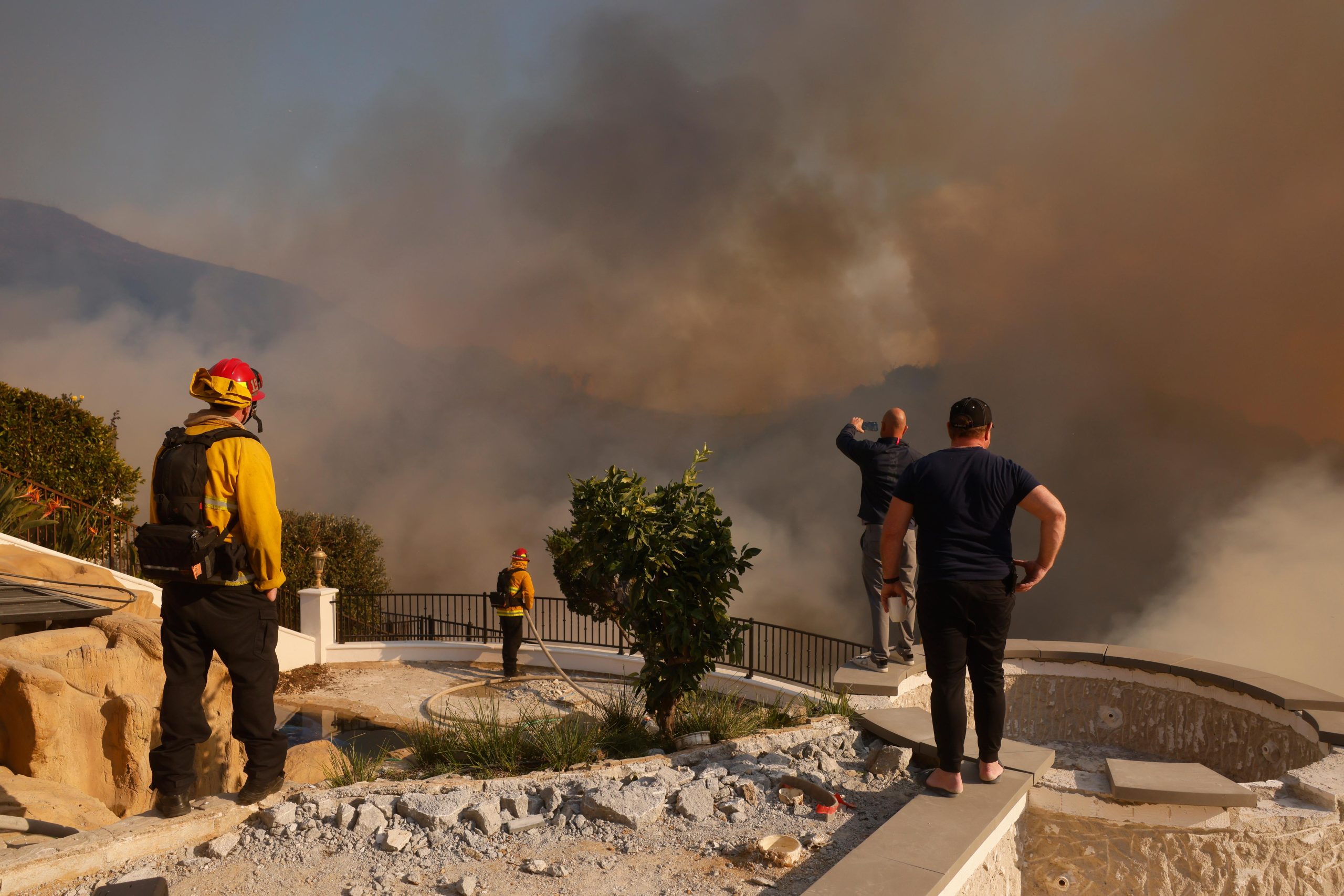 Residents and firefighters watch as the Palisades Fire advances in...